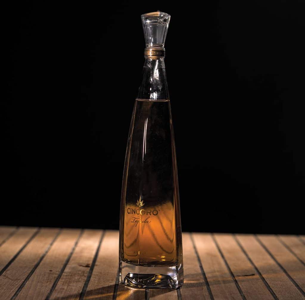 Cincoro Añejo Tequila on a wooden table with a black background.