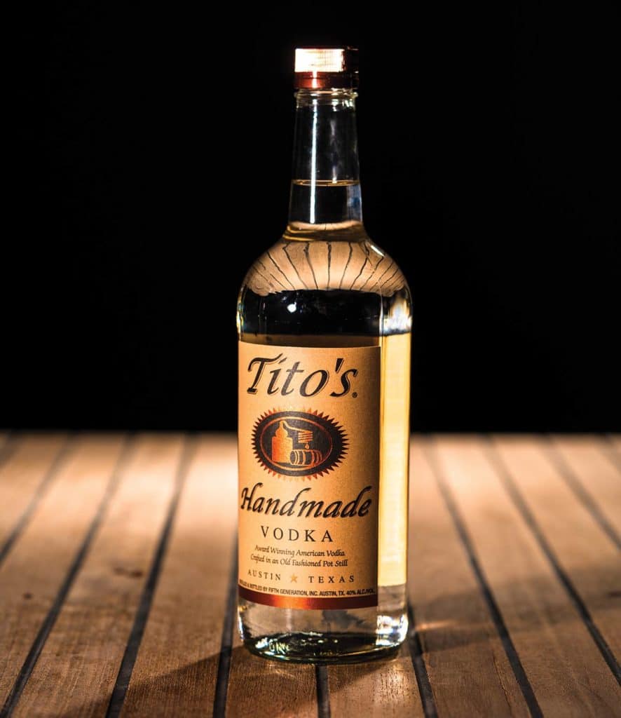 Tito’s Handmade Vodka on a wooden table and black background.