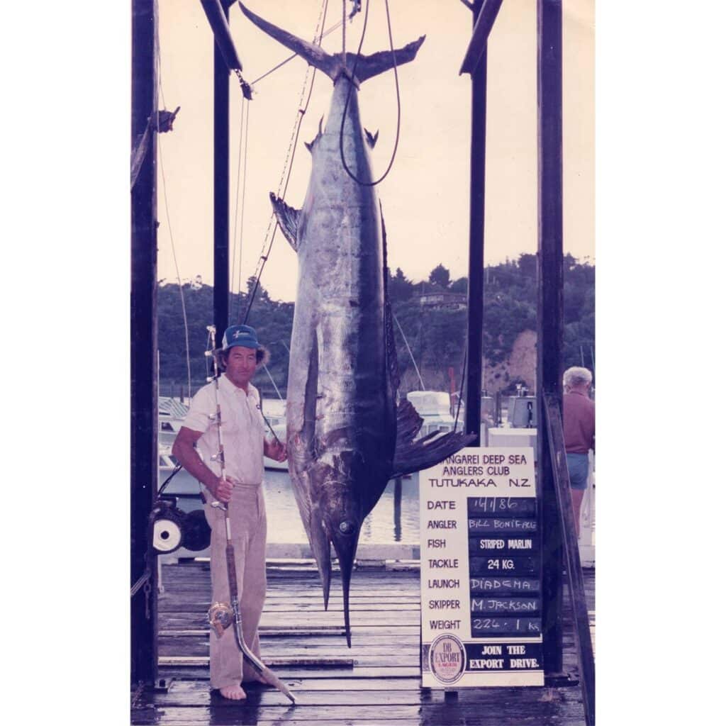 Bill Boniface standing next to a large striped marlin being weighed at the docks.