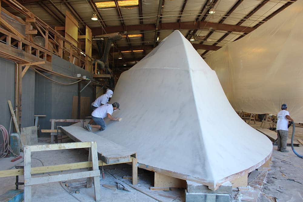 fairing team smoothing out a boat hull under construction