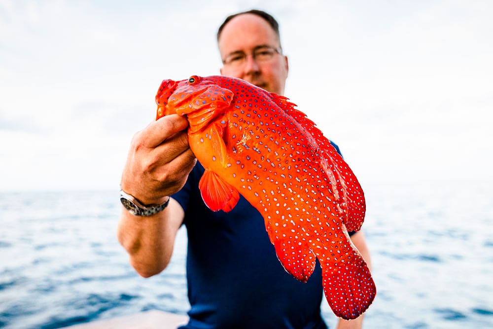 man holding up a red and yellow-spotted fish
