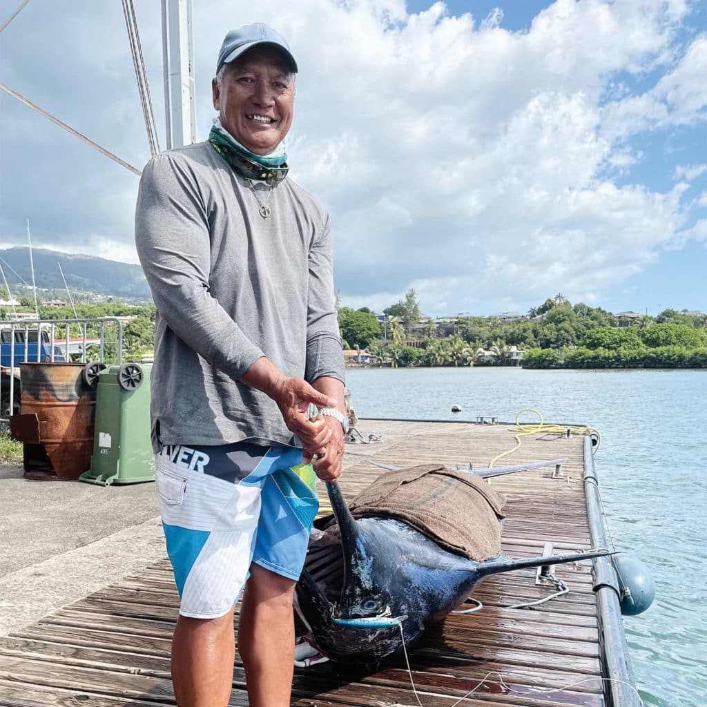 A man stands on a dock next to a large blue marlin.