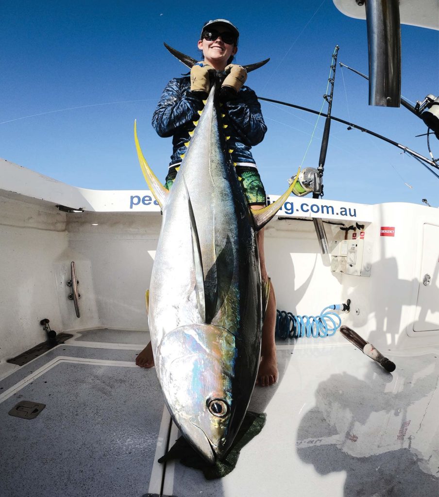 An angler holds a large yellowfin tuna up in the deck of a sport fishing boat.