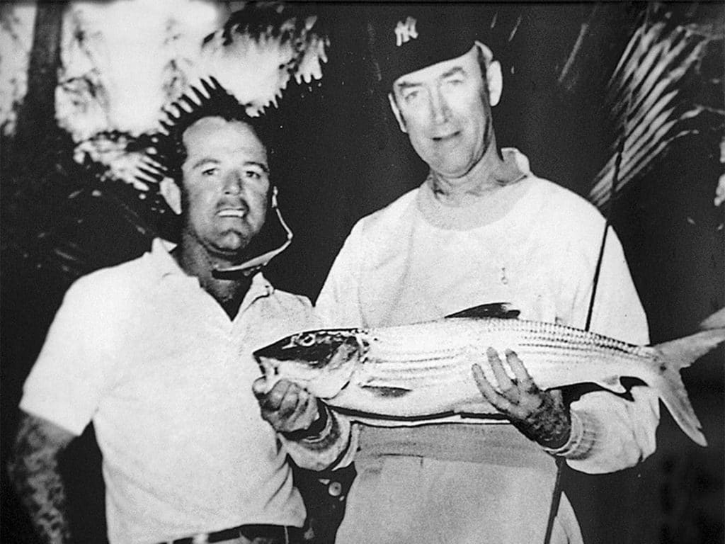 A black and white photo of two men, one holding a fish.