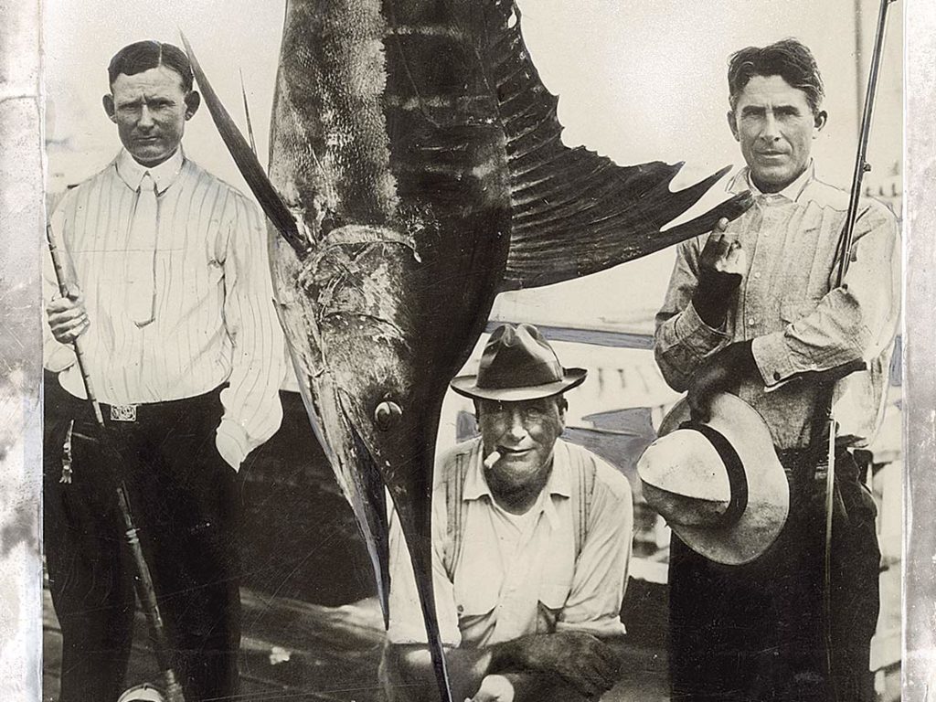 A black and white image of three men standing beside a large marlin.