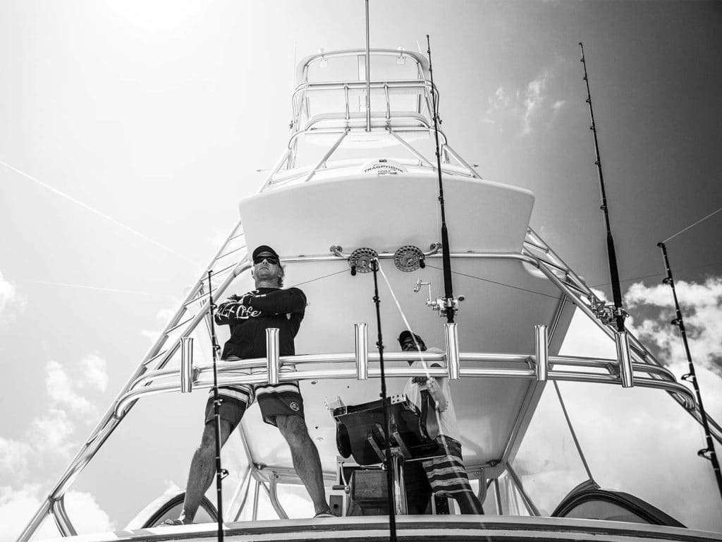 Black and white image of a man standing in a sport fishing boat cockpit.