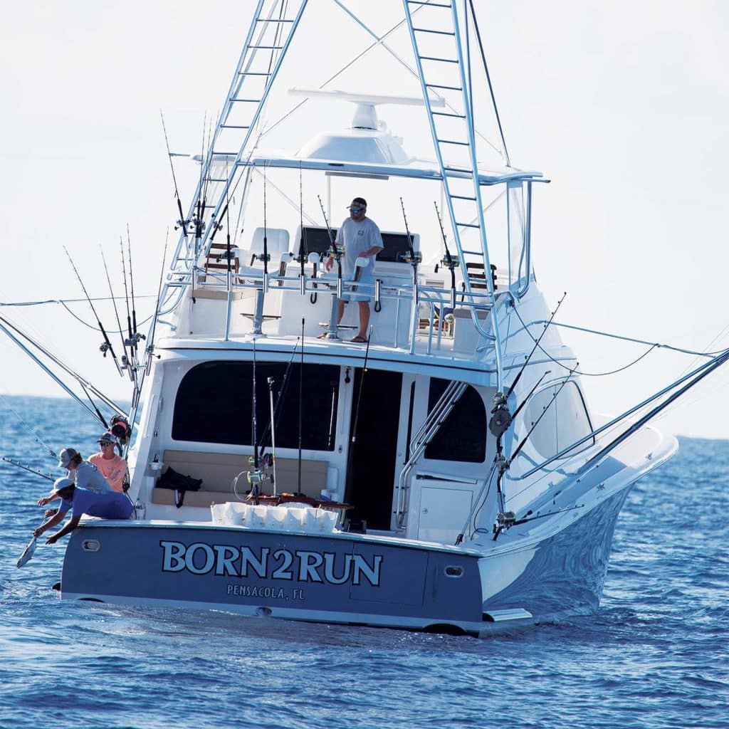 A sport-fishing boat on the water, with crewmen fishing and checking equipment.
