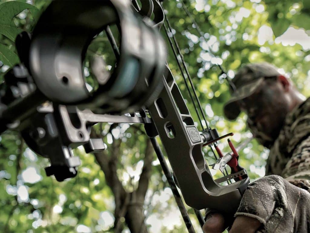 A bowhunter draws back on a bow and peers through the targeting sight.