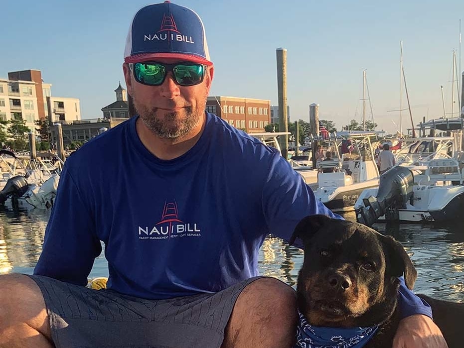 A man sits on a boat deck with their dog.