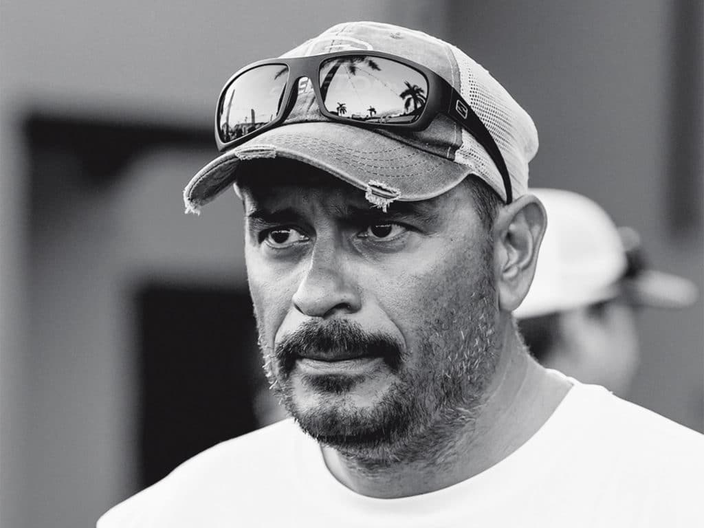 Black and white image of a man wearing a cap and sunglasses.