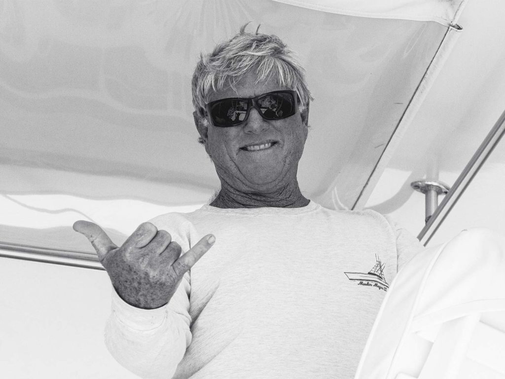 A black and white image of a boat captain wearing sunshades.