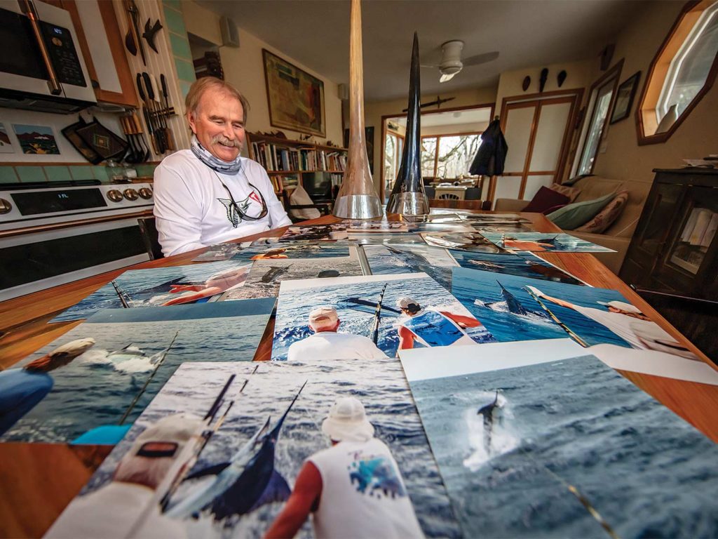 A man sits by a table covered with photographs of his notable catches.