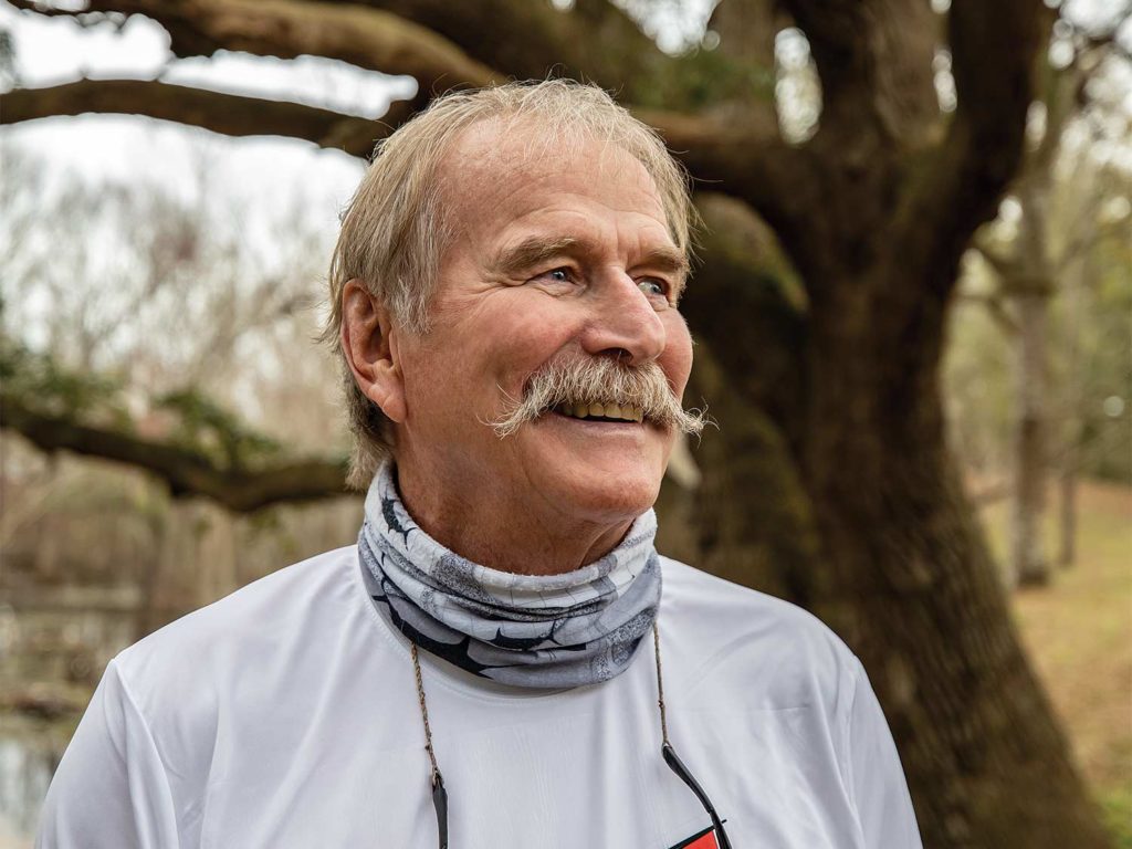 A man smiles and stands beside a tree.