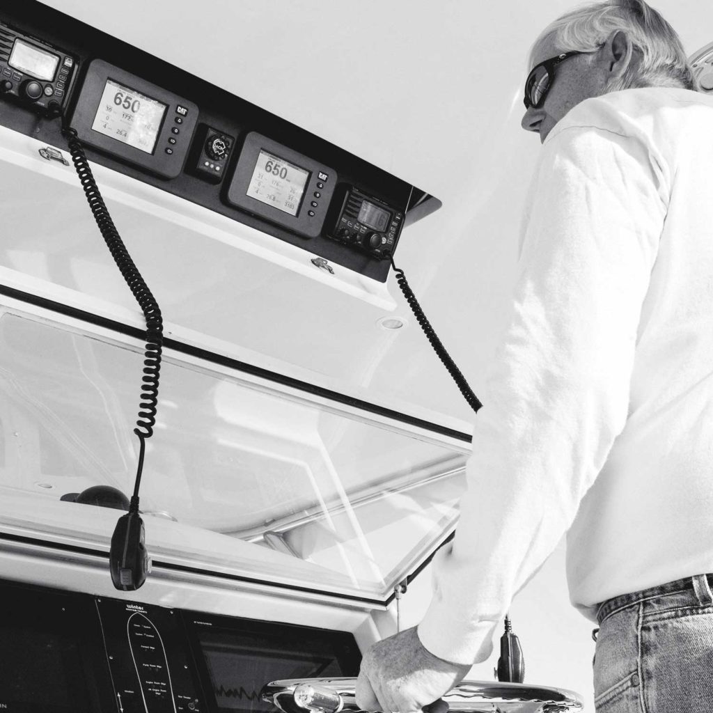 A black and white image of a boat captain at the helm of a sport-fishing vessel.