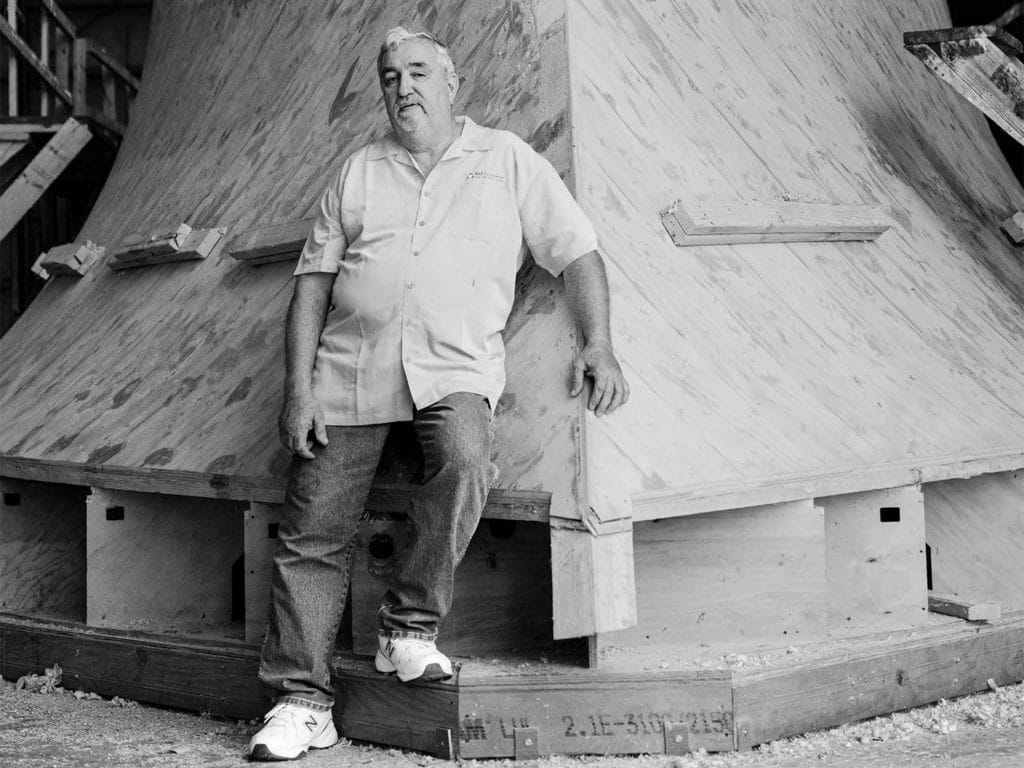 A black and white photo of a man leaning against a sport fishing boat hull.