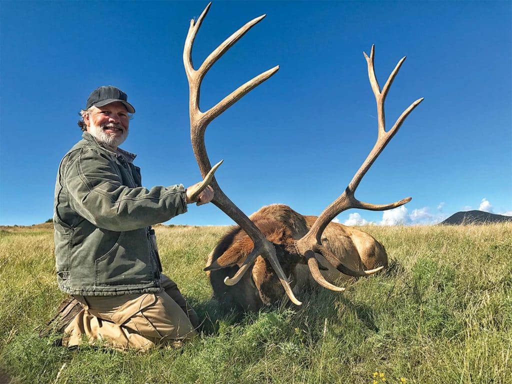 A hunter kneels beside a dropped elk.