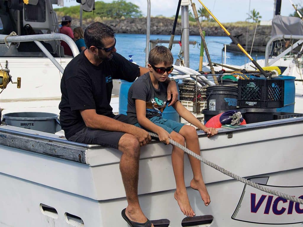 A father and son sit on the transom of their sport fishing boat.