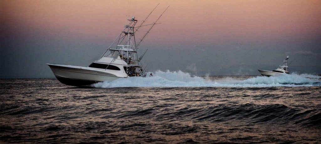 two sport fishing boats cutting through the water at sunset