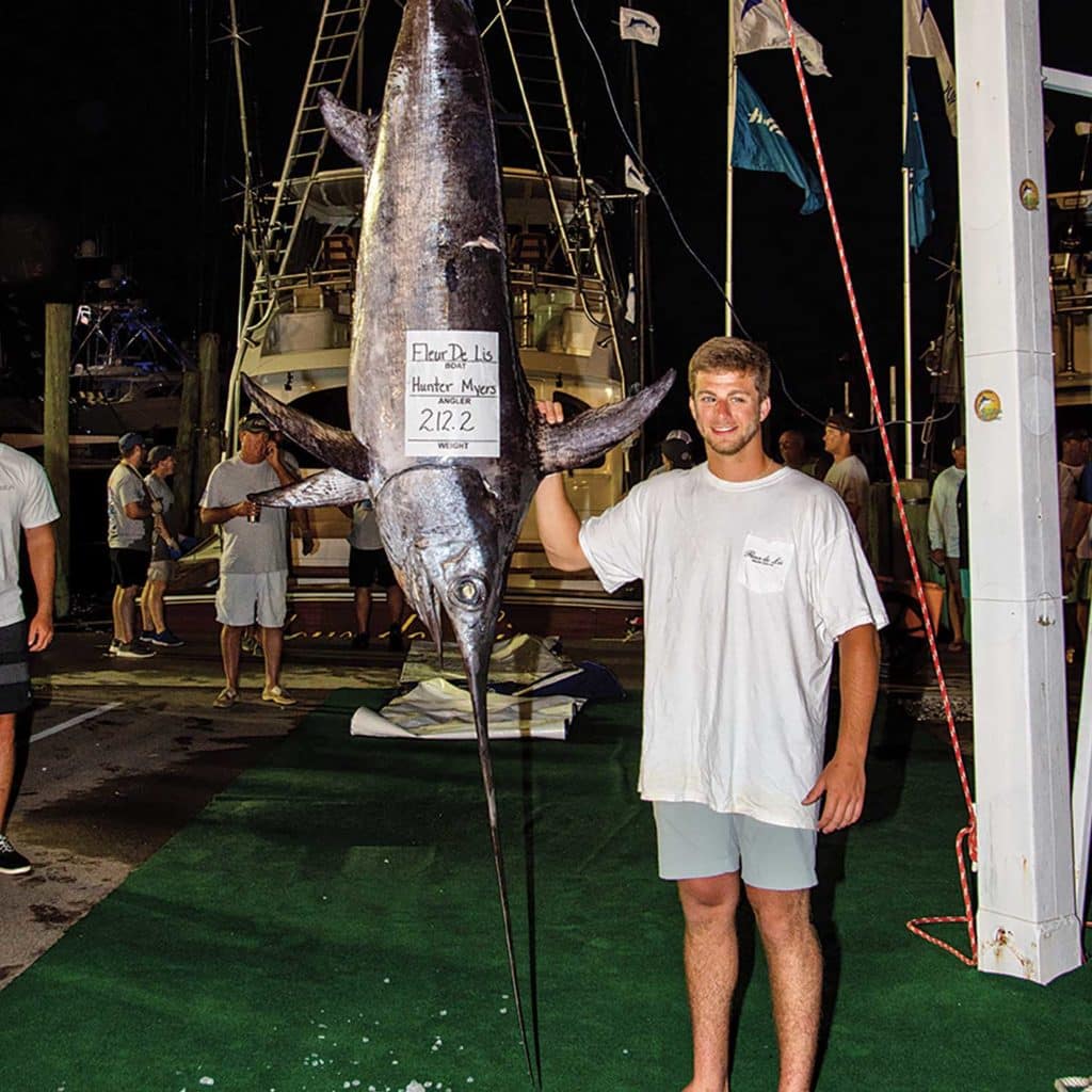 A young man stands next to a large swordfish.