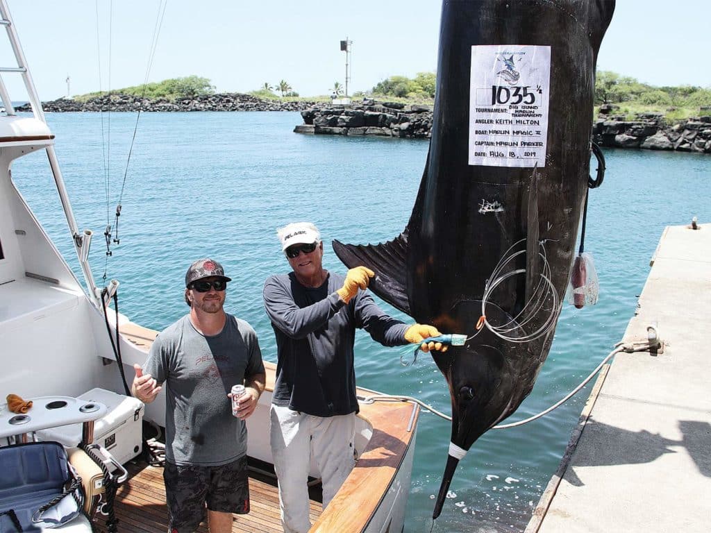 Two men stand on a boat deck next to a large blue marlin.