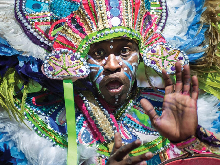 A Junkanoo parade participant in full costume and face paint performs in a parade.