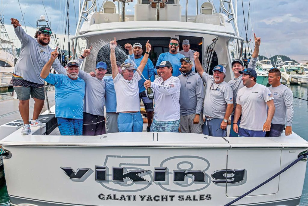 A sport-fishing team stands on a boat's cockpit and celebrates a win.