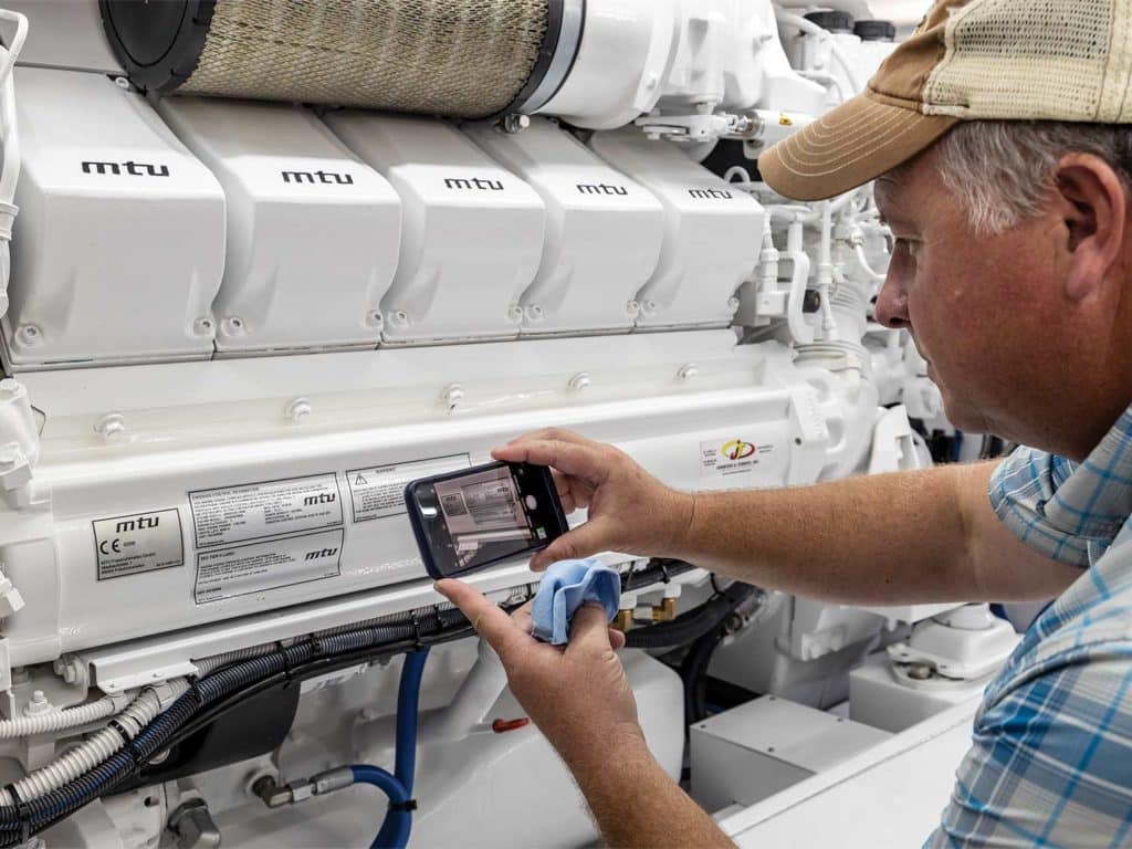 A man inspects an engine and takes a photograph of the labeling with his phone.