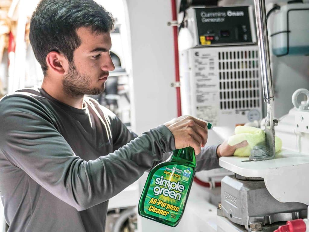 A young man cleans a boat engine room with simple green all purpose cleaner.