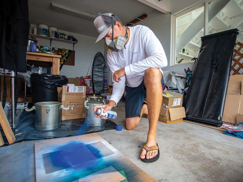 A man sprays custom boards with blue spraypaint.
