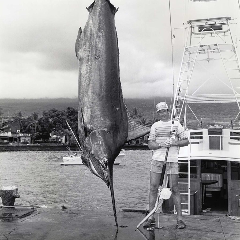 A black and white image of a man standing next to an IGFA world record blue marlin.