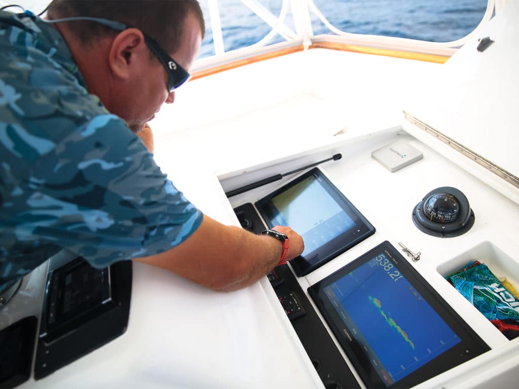 A man touches an electronic display panel at the helm of a sport fishing boat.