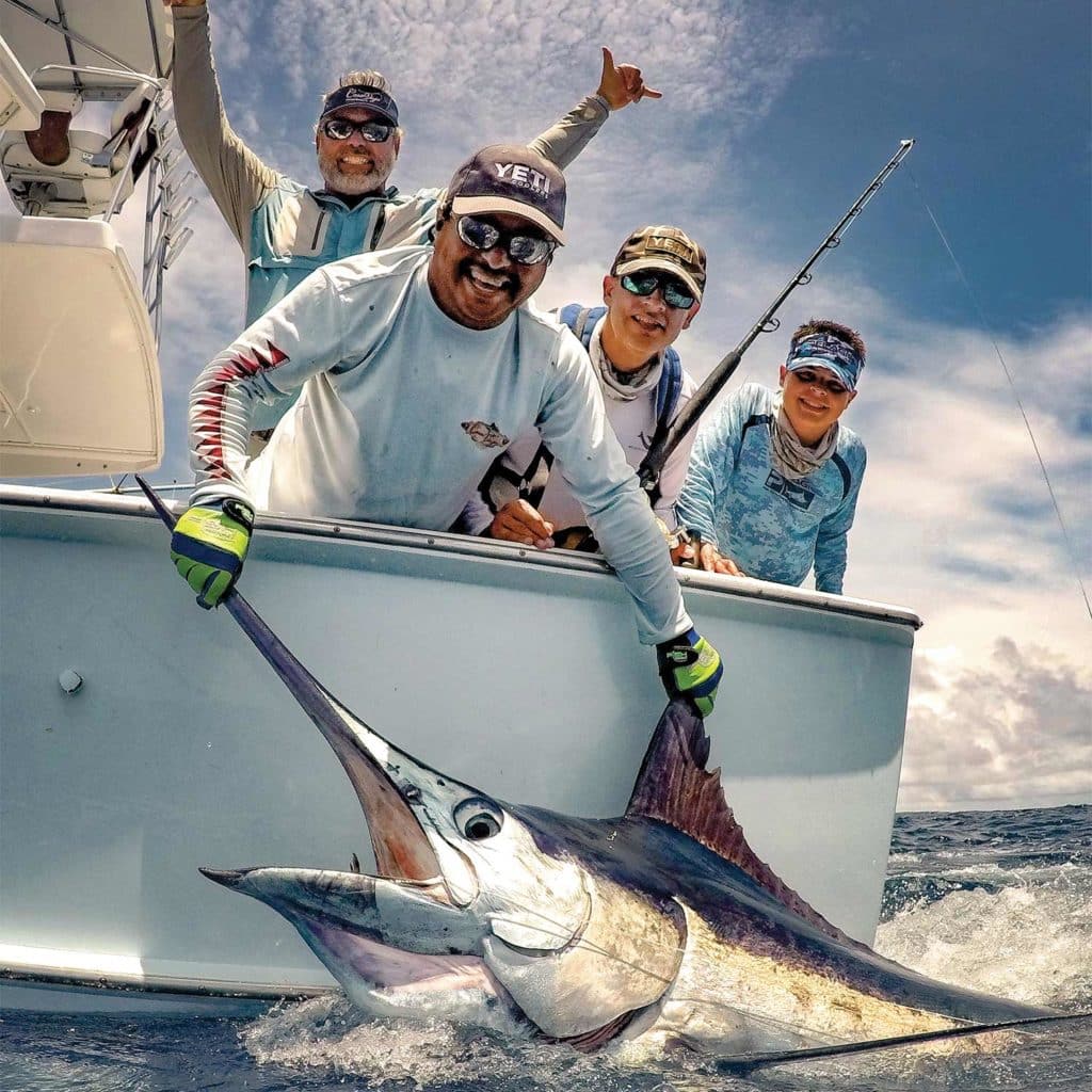 a sport fishing team holding a marlin boatside