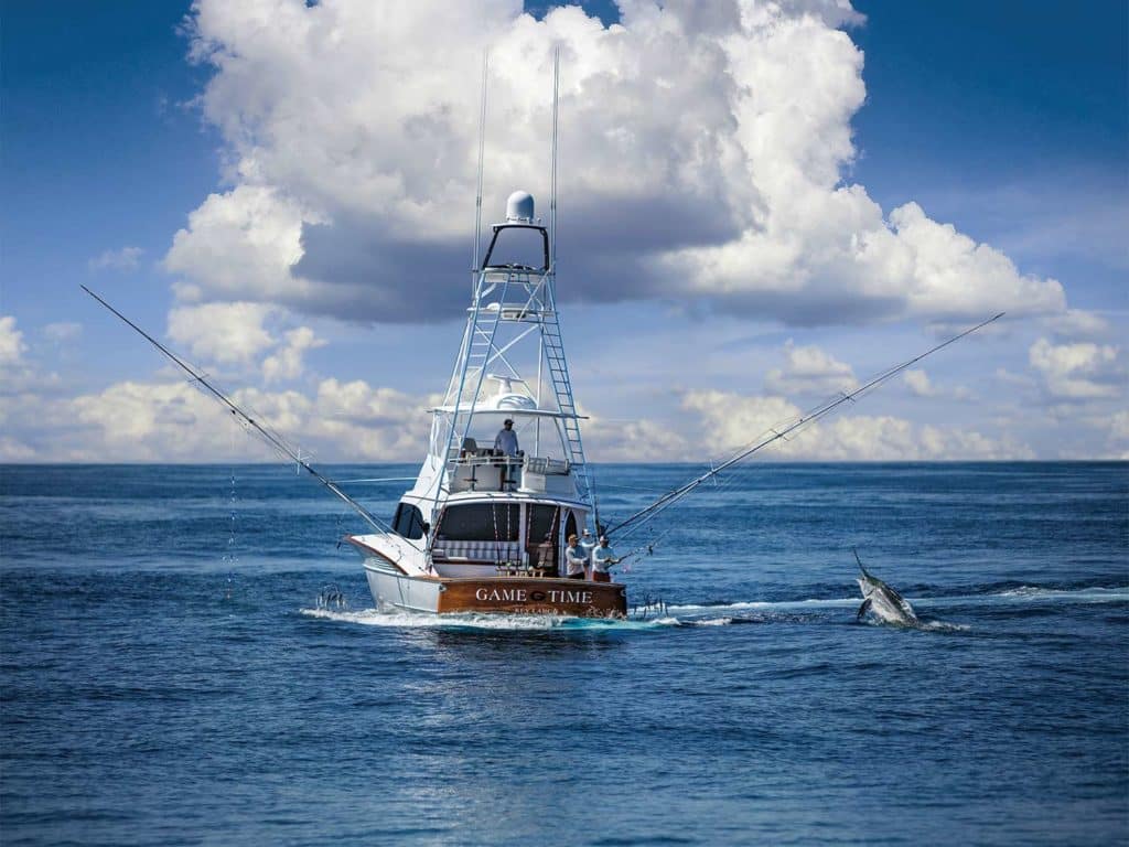 A sport fishing boat on the water while a fishing team reels in a large marlin.