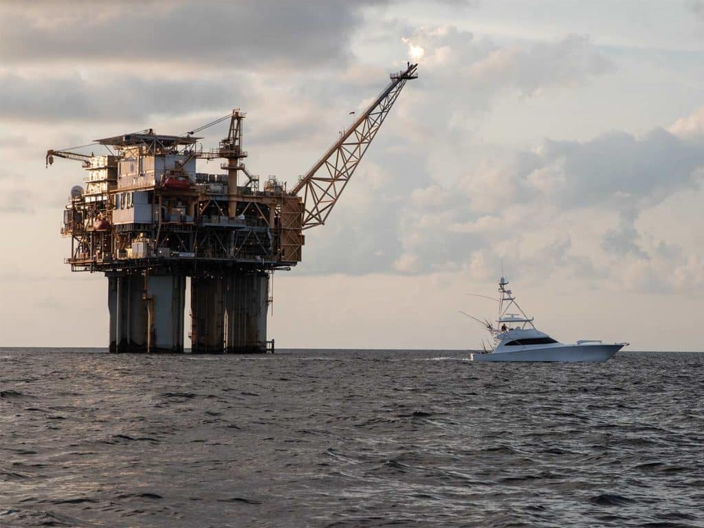 A sport-fishing boat sails past an oil rig in the ocean.