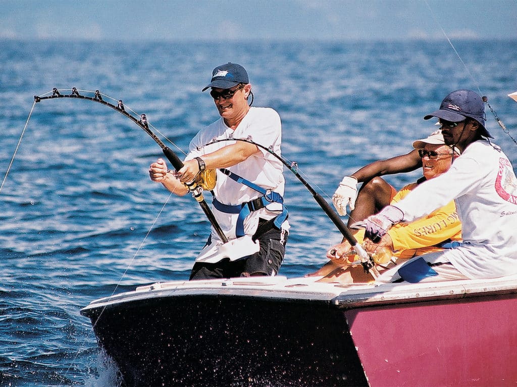 A team of sport fishing anglers reeling in a large marlin on a boat deck.