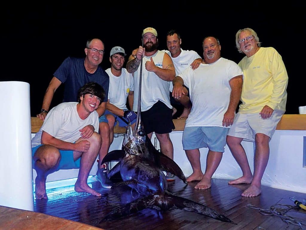 A group of sport-fishers standing around a swordfish.