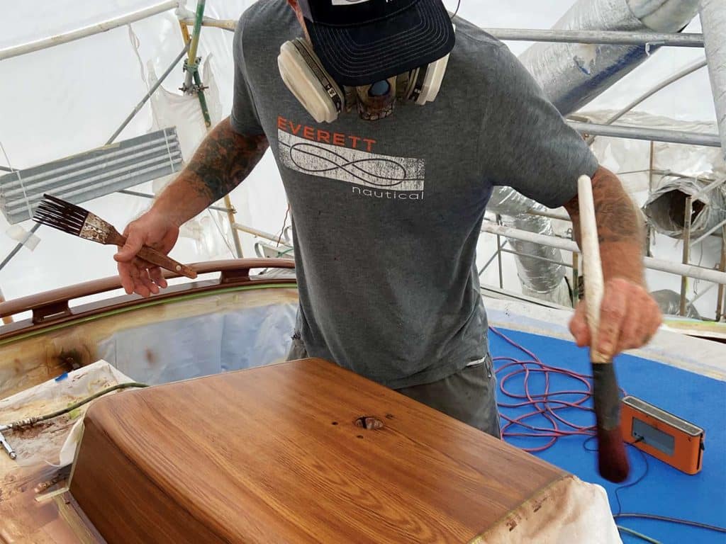 A man paints and stains a piece of wood.