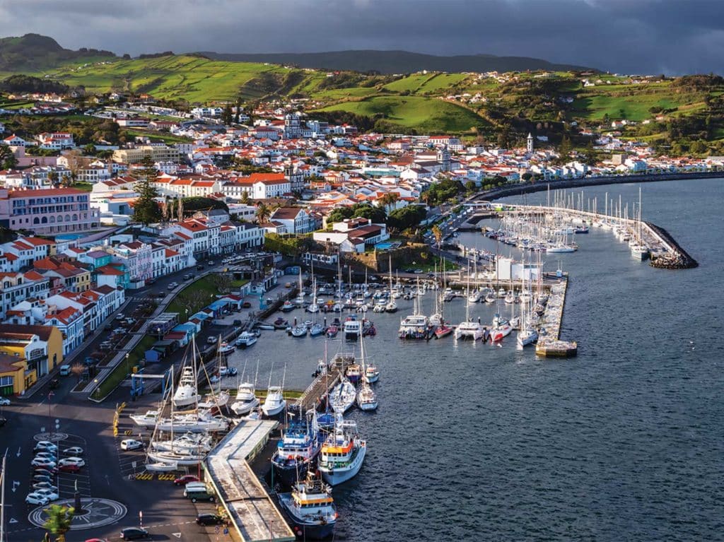 The bay town of The Azores. The city is full of white building with red roofs. The waterfront is lined with sport-fishing boats docked in harbors.
