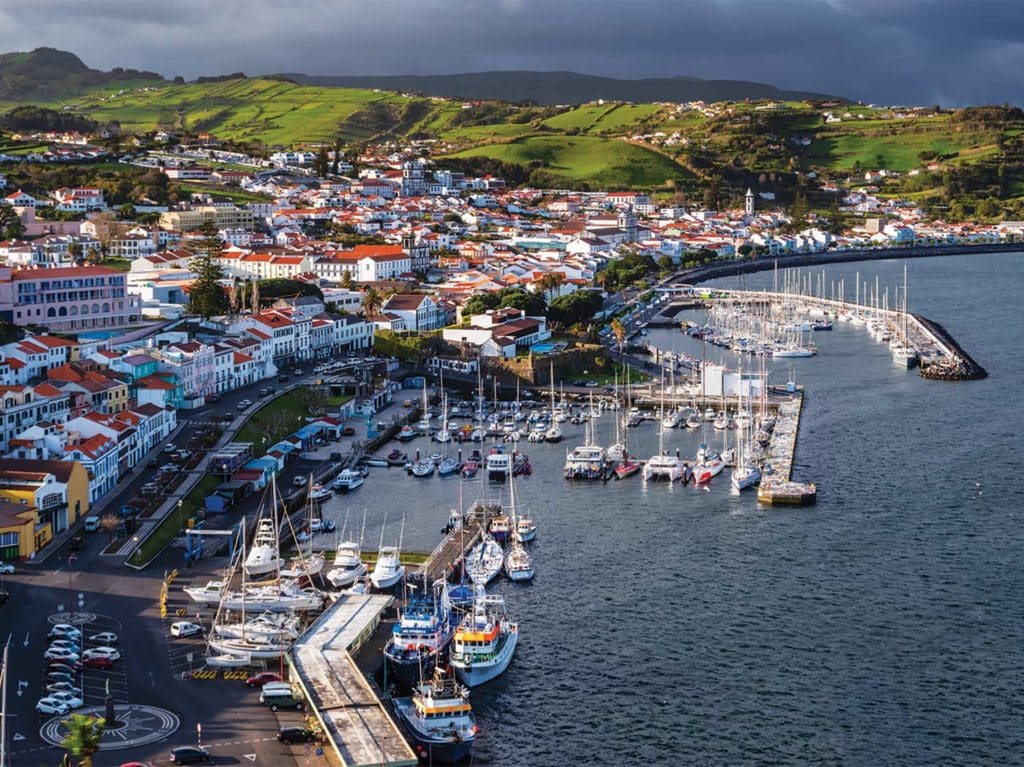 The bay town of The Azores. The city is full of white building with red roofs. The waterfront is lined with sport-fishing boats docked in harbors.