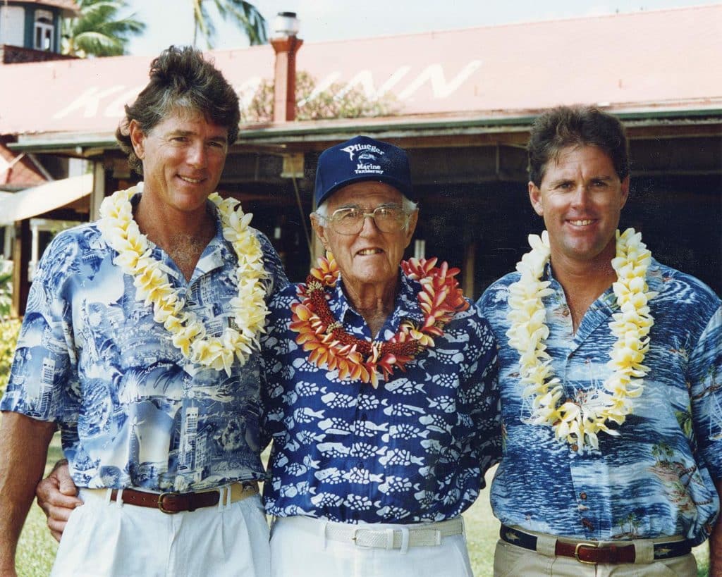 Three mean stand together and wear tropical shirts and lei flower necklaces.