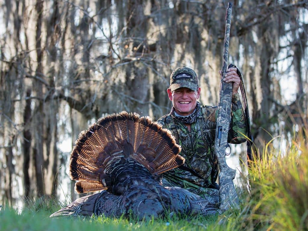 A hunter kneels beside a dropped turkey.