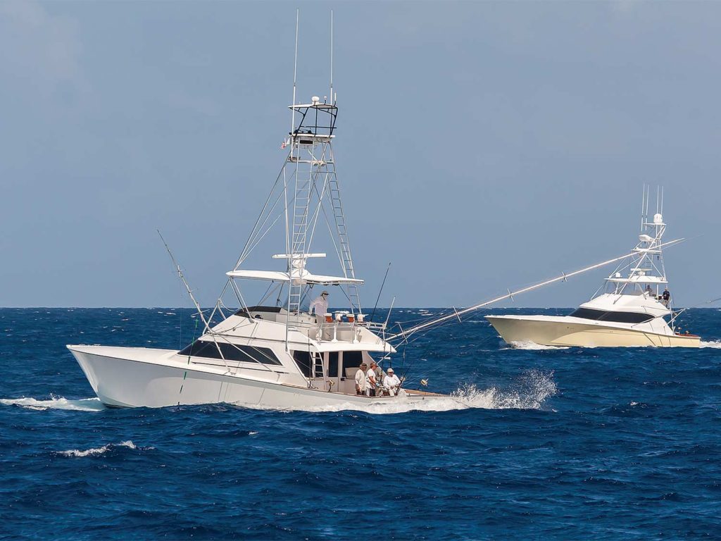 Two sport fishing boats on the water. Their teams are fishing off the decks.