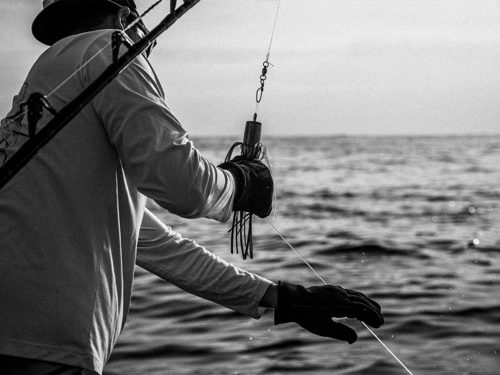 Black and white image of a wireman holding a marlin lure and a lead wire.