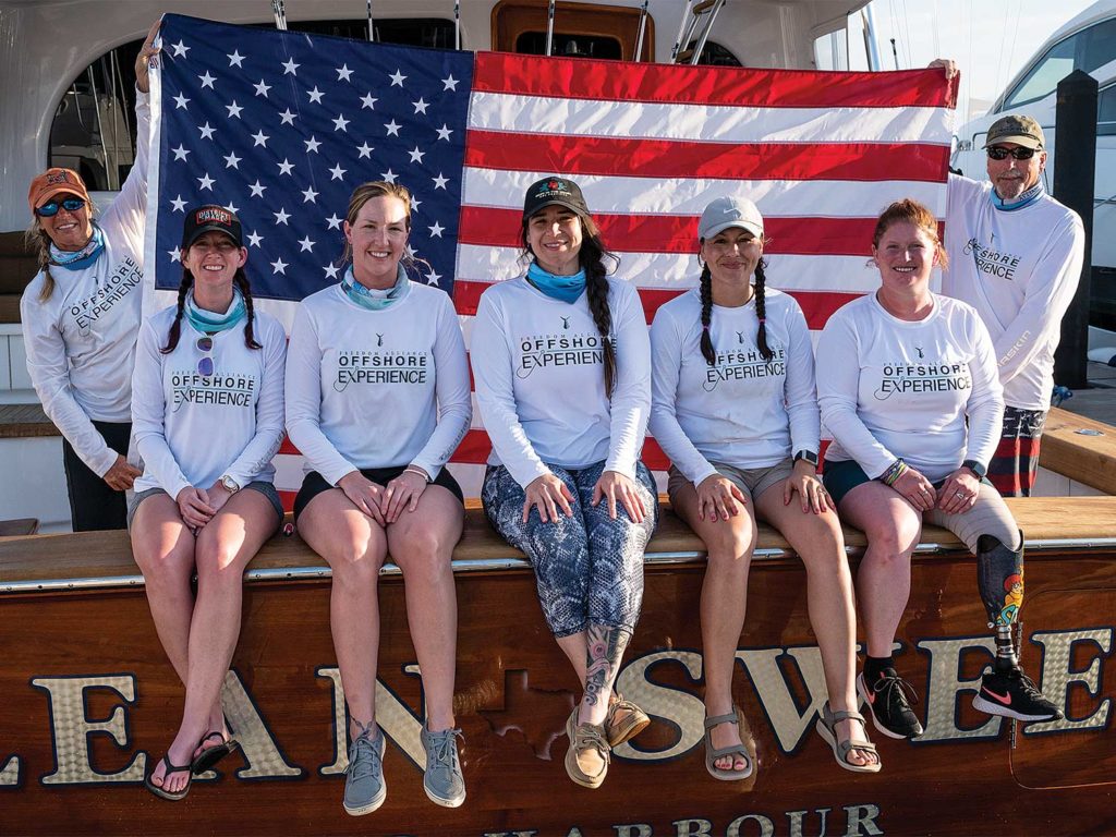 A group of seven women sitting on the transom of a boat.