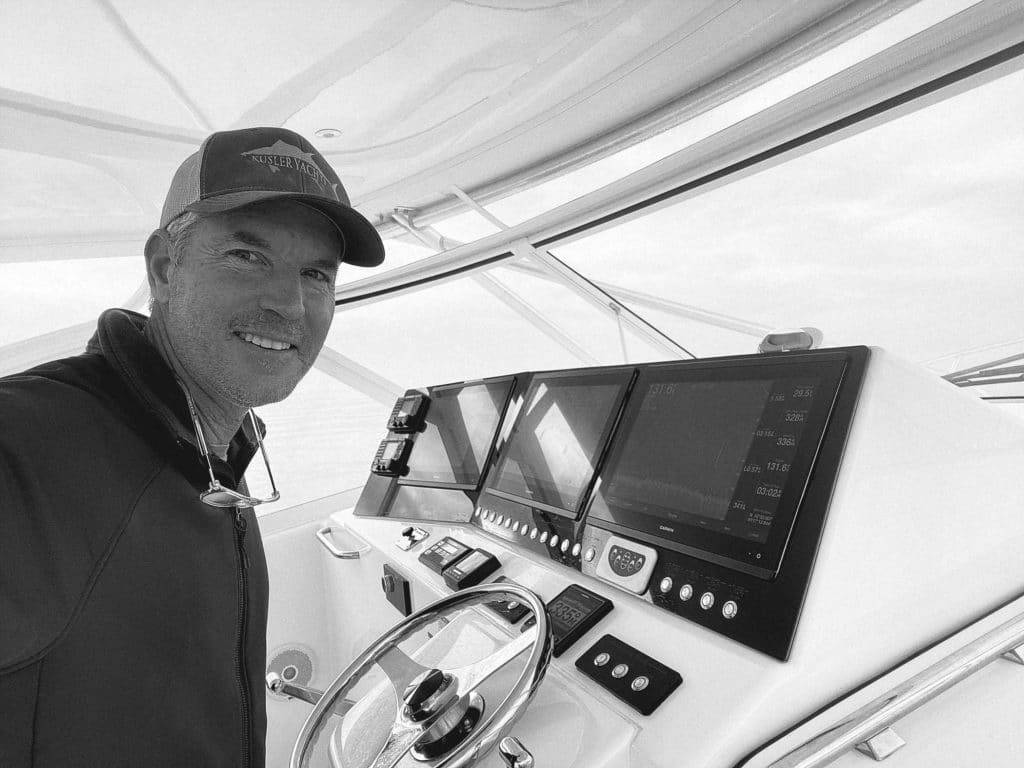 A black and white image of a man at a sport-fishing boat helm.