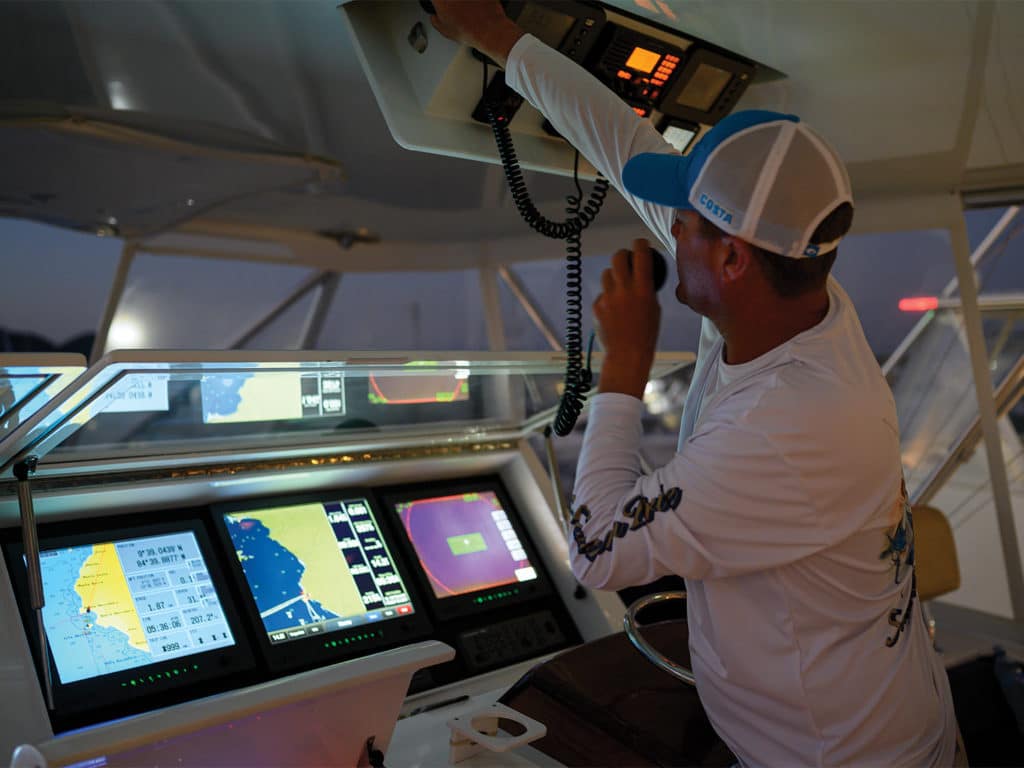 A boat captain at the helm surrounded by marine electronic displays.
