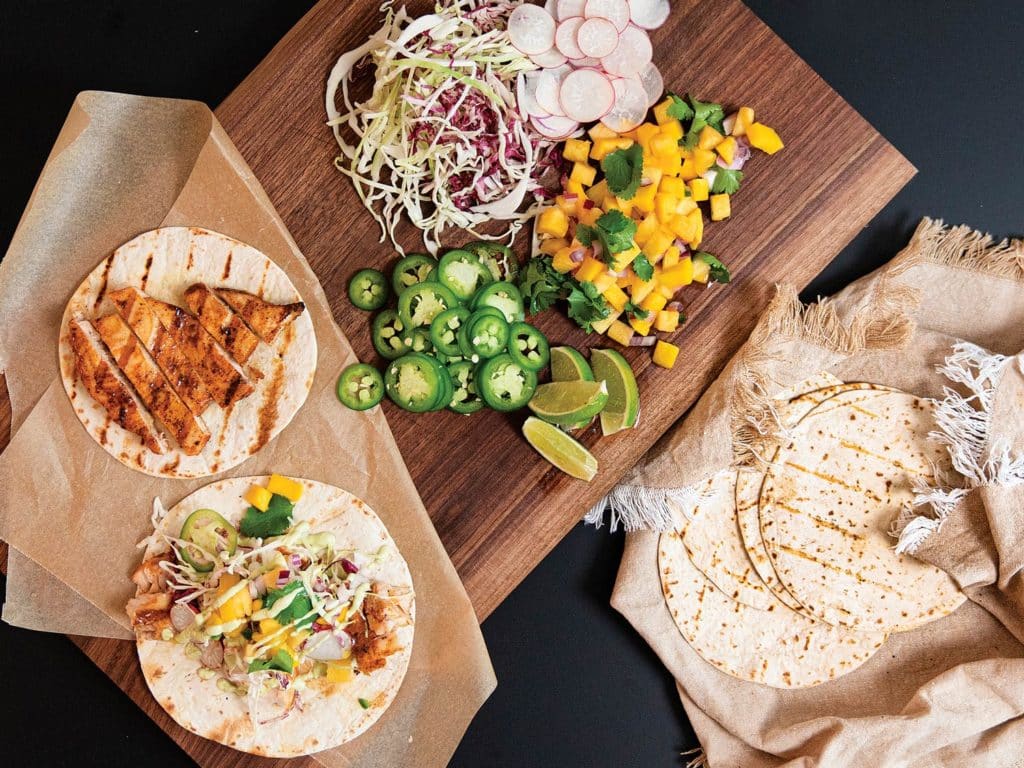 An arrangement of swordfish tacos and various toppings and dressings.