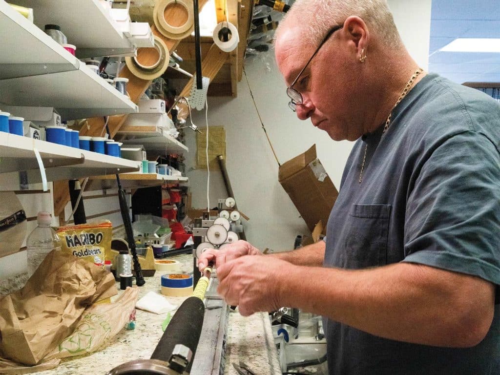 A man shapes a custom fishing rod in a workshop.