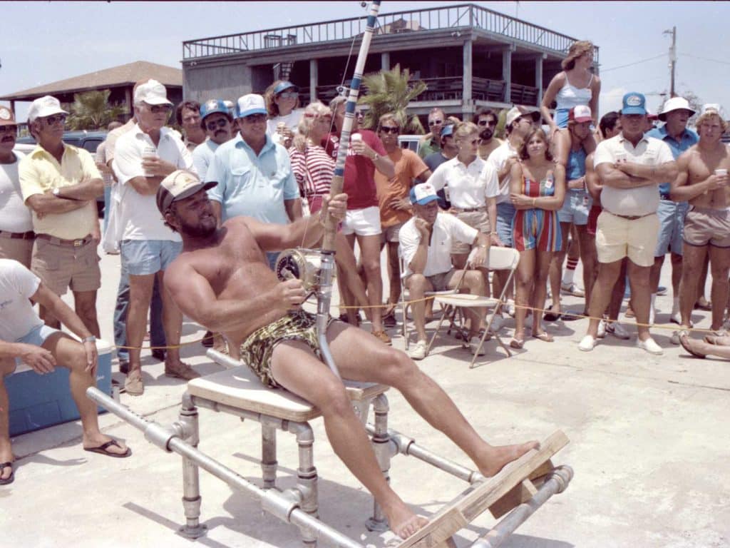 A man sitting in a fighting chair as onlookers watch him compete.