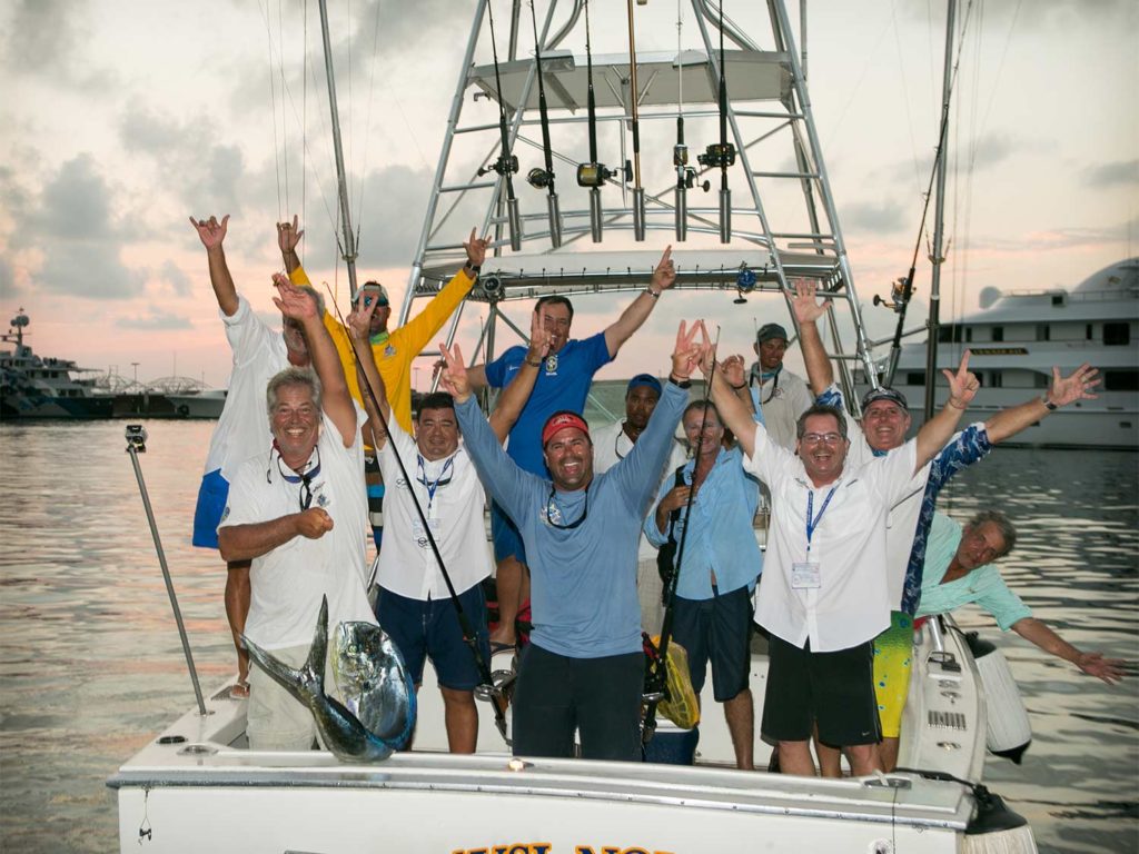 A fishing team standing in the cockpit of a boat, arms up in celebration.